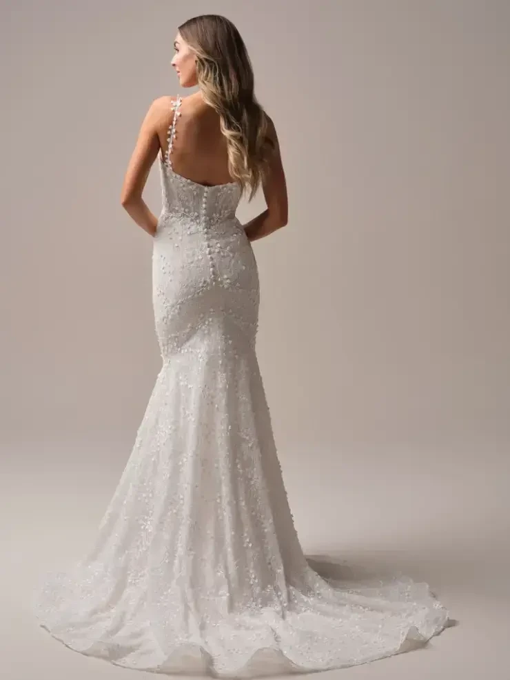 A woman wearing a fitted white wedding dress with embellished details, viewed from the back.