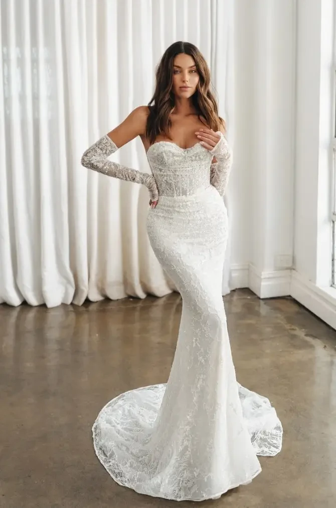 Model is wearing a strapless fit-and-flare lace wedding dress with detachable long lace gauntlet sleeves.