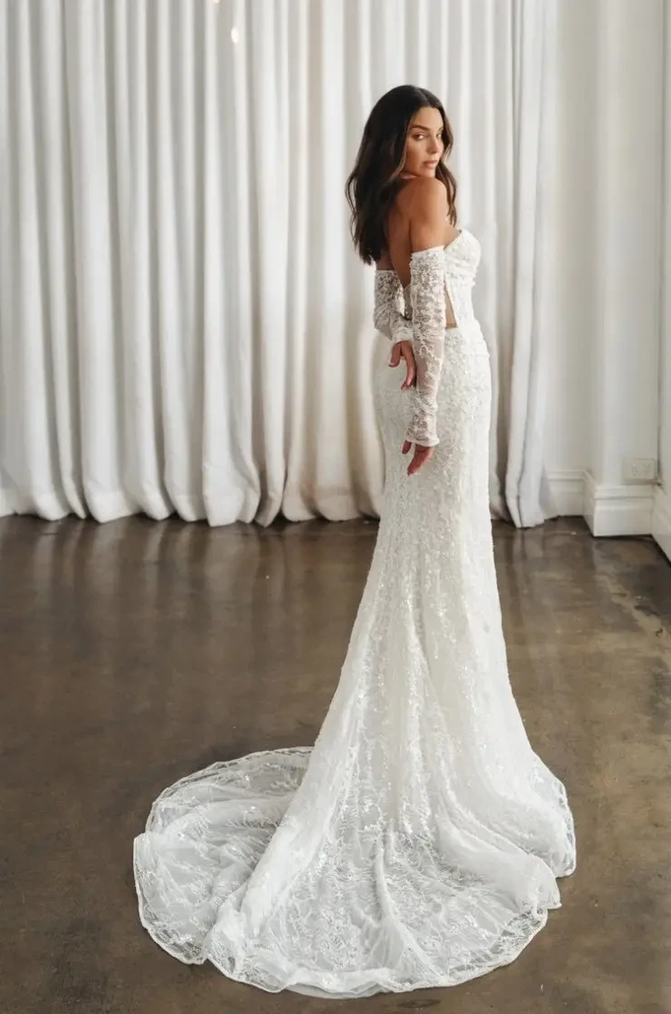 Model is wearing a strapless fit-and-flare lace wedding dress with detachable long lace gauntlet sleeves.
