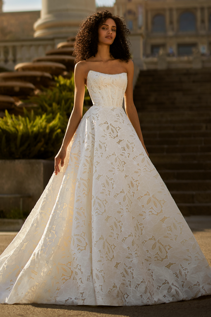 Model is wearing a strapless ball gown with a sweetheart neckline, sheer corset bodice, and exposed boning detail.
