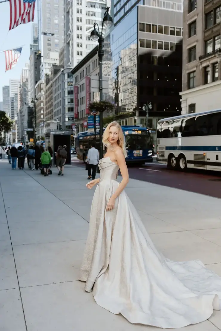 Model is wearing a shimmering light gold ball gown with a ruched cat-eye bodice and a full, dramatic skirt.