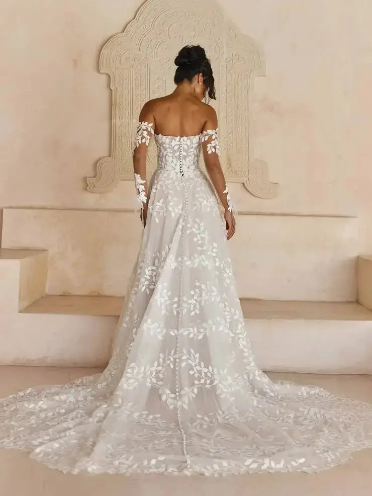 Model is wearing a strapless a-line wedding gown with detachable off the shoulder sleeves and a leaf lace pattern 