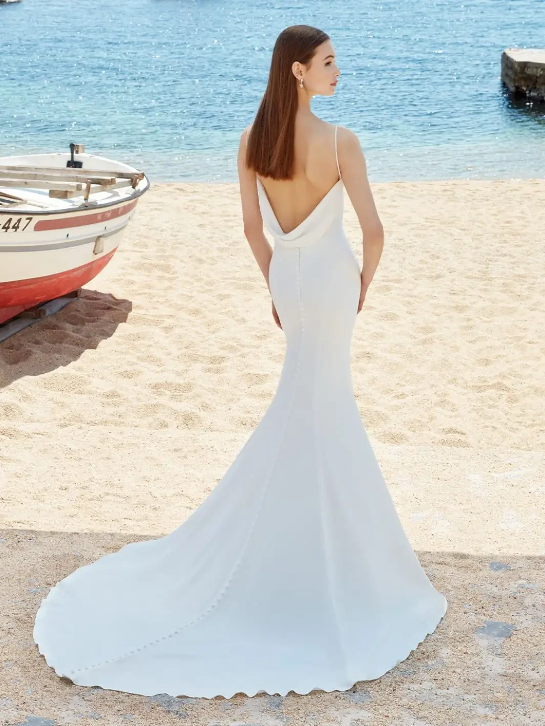 Model is wearing a minimalist georgette gown with spaghetti straps, a draped open back, and a long train.