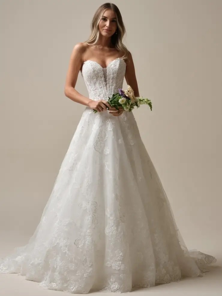 Model is wearing an a-line wedding dress with a plunging basque waist and off the shoulder neckline