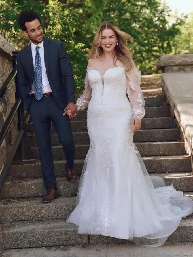 A couple walking down stone steps; the woman is wearing a white wedding dress and the man is in a dark suit.