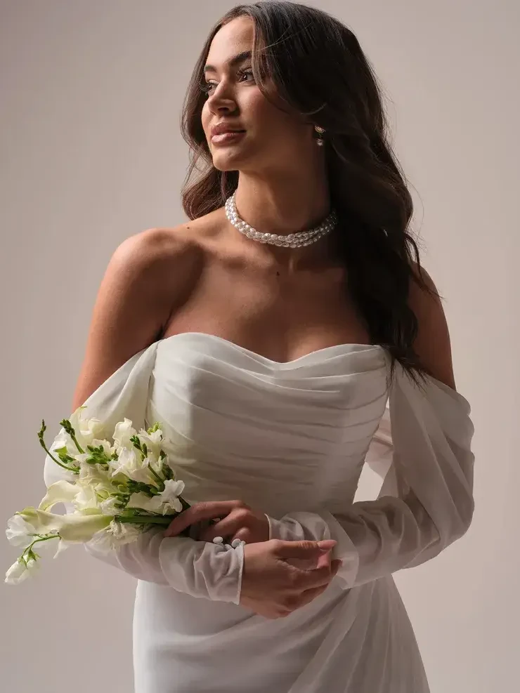 model is wearing an off the shoulder long sleeve wedding dress
