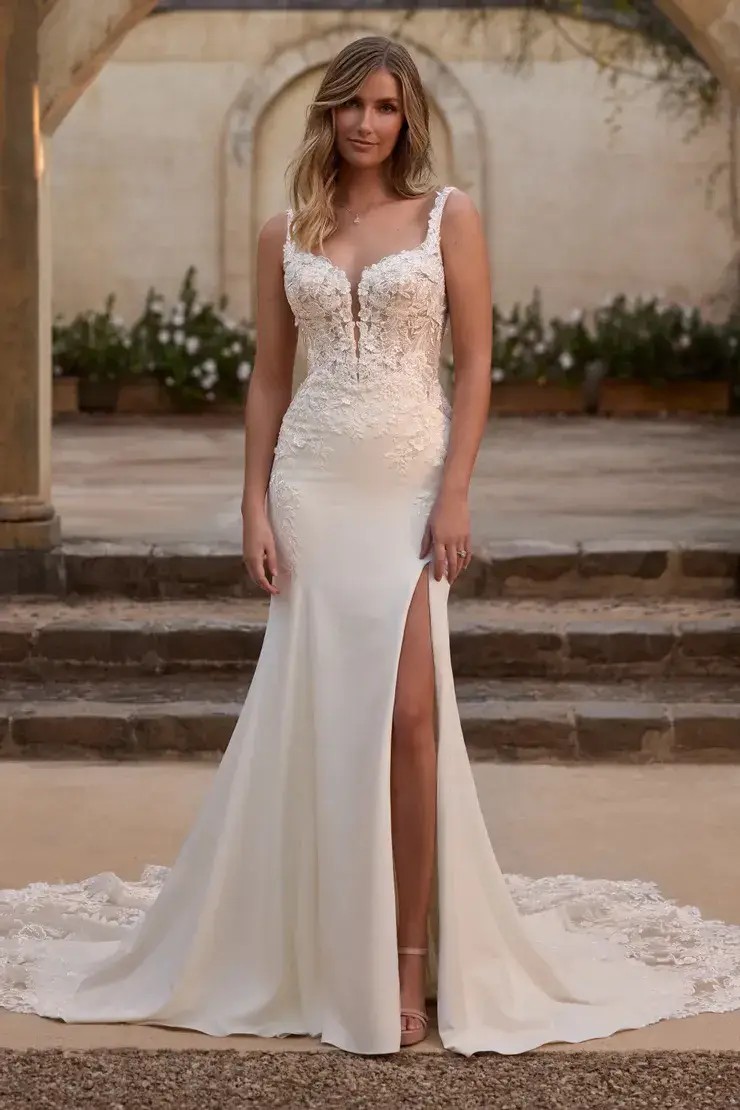 Model is wearing a fit and flare bridal gown with a slit, plunging neckline, and beaded lace appliques 